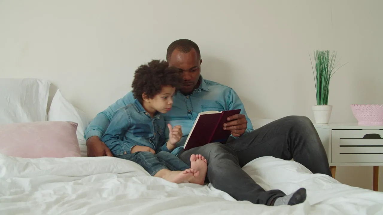 A father and son reading together on a bed
